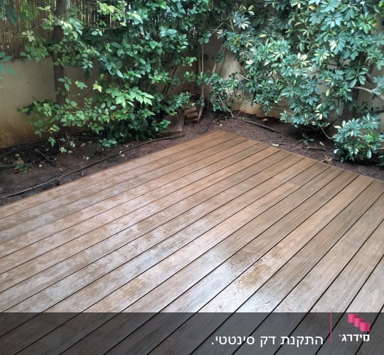 דק עץ בגינה עם צמחייה ירוקה מסביב
